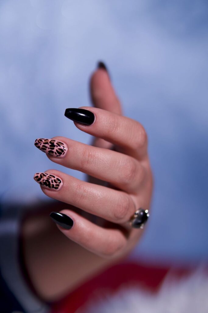 10 Easy Nail Art Ideas for Beginners You Can Try at Home 2 A hand against a dark red background showing bright pink manicured nails with black tips and decorative accents. This Easy Nail Art design combines vibrant pink with contrasting black details.