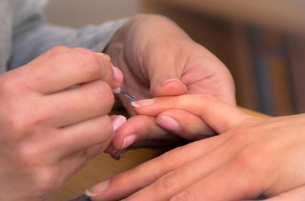Close-up of hands during a manicure preparation for applying burgundy nail polish.