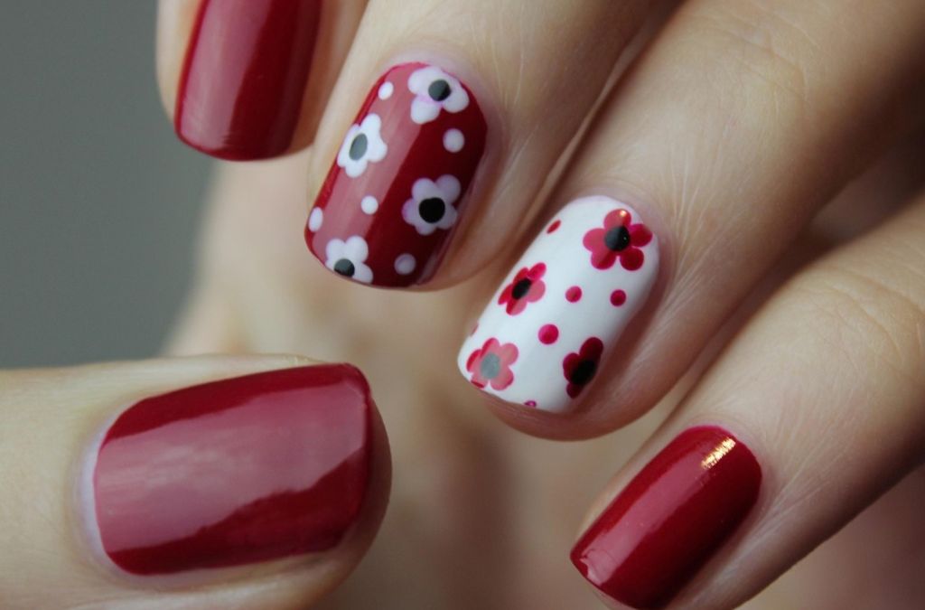 Burgundy nail polish with white accent nails featuring red flowers and polka dot nail art.