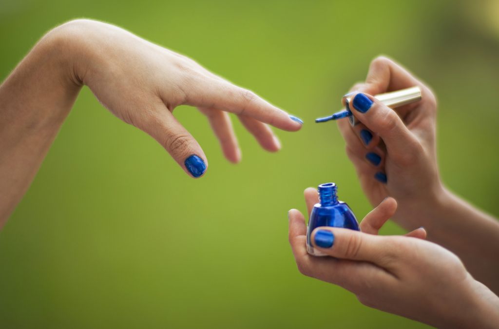 Person applying blue nail polish outdoors as an alternative to burgundy nail polish.
