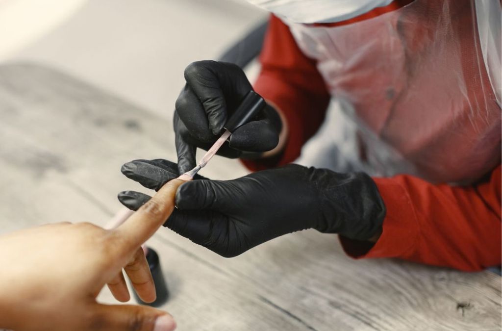 Nail tips nails application performed by a nail technician wearing black gloves.