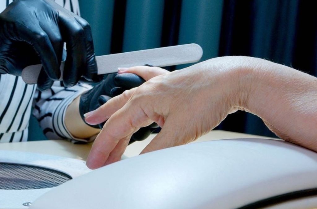 Nail polish on gel nails preparation using a professional nail filing machine.
